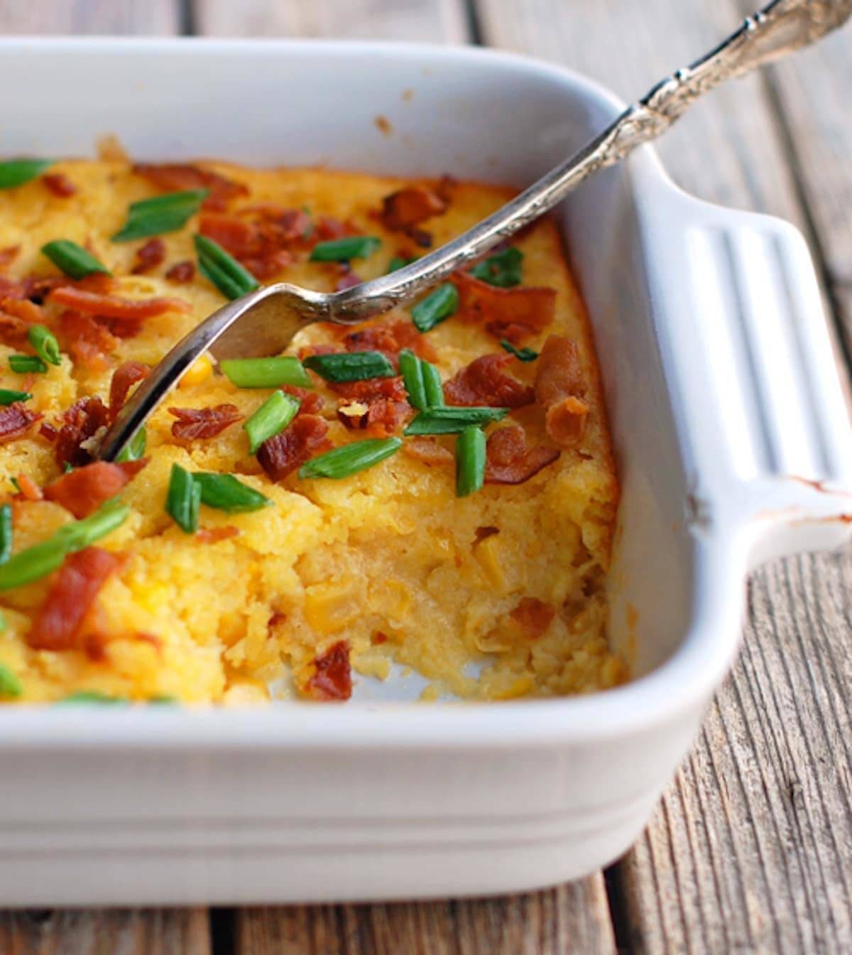 Creamy baked corn  with a spoon in a white baking dish.