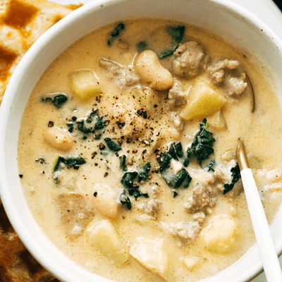 Sausage, kale, and bean soup in a bowl with a spoon.