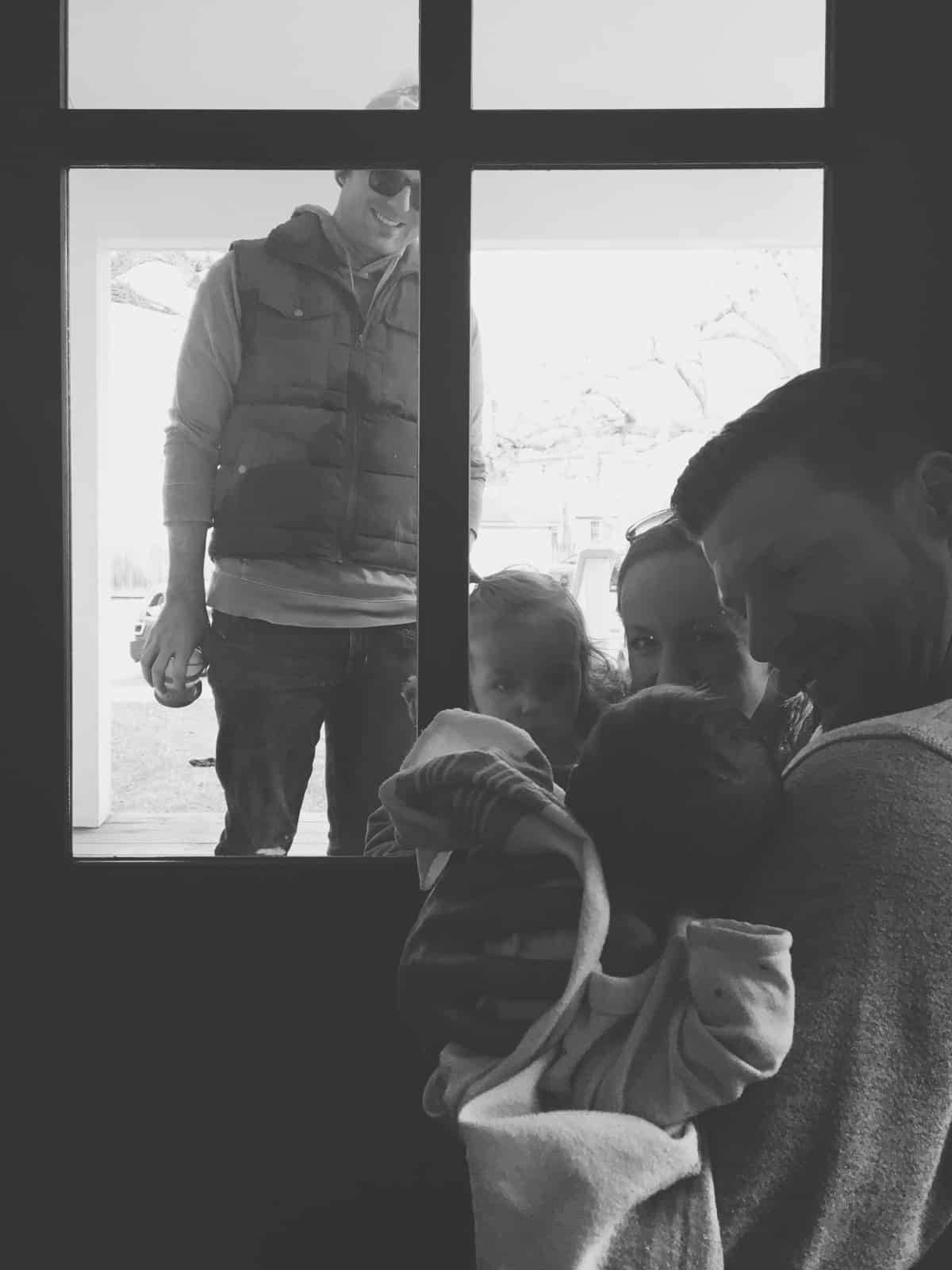 Two families social distancing and talking to each other through a door. 